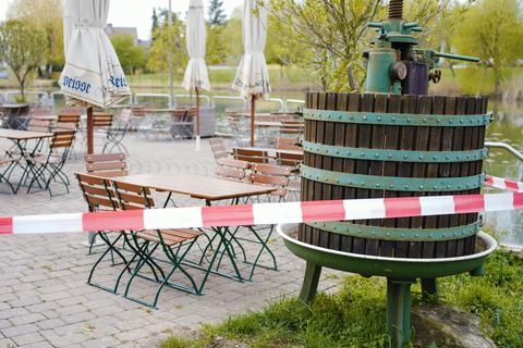Ein Absperrband hängt um eine Terrasse mit leeren Tischreihen und einer Weinpresse am Haus der Deutschen Weinstraße. Foto: dpa