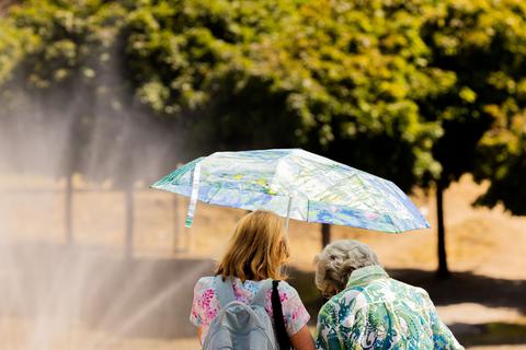 Zwei Frauen schützen sich in der Sonne mit einem Regenschirm vor der Hitze.