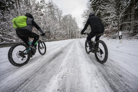 Zwei Mountainbiker sind mit ihren Rädern auf einer schneebedeckten Straße unterwegs. Im Winter sind die Straßen auch für Fahrradfahrer nicht ungefährlich.  Foto: dpa